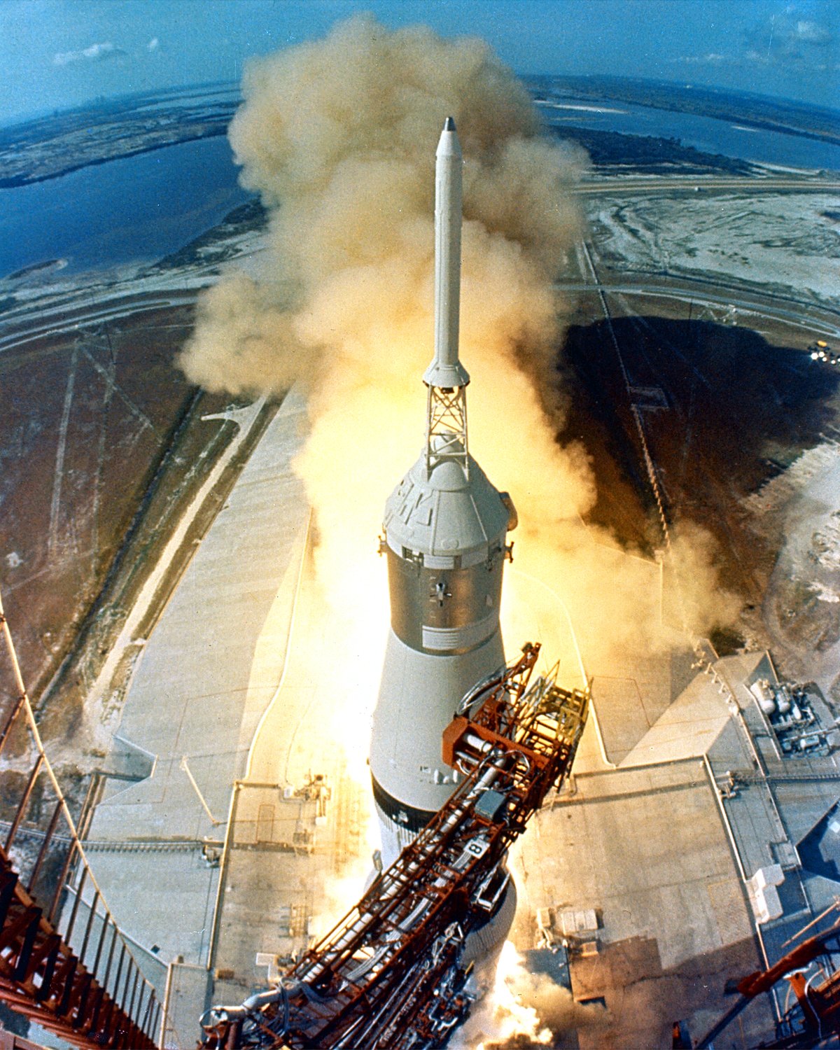 1969年7月16日、アポロ11号を載せたサターンVロケットが、発射台から上昇している。白い機体の下から、炎と煙が広がる。ケネディ宇宙センターで、NASAが撮影した写真。
